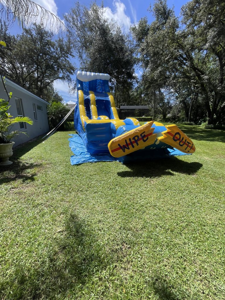 A huge inflatable water slide with a broken surfboard with words 