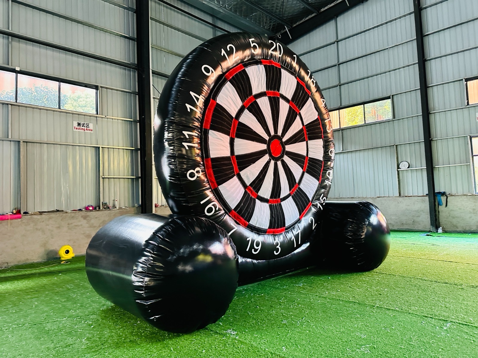 A large inflatable Soccer Dart game set up on artificial grass inside a warehouse.