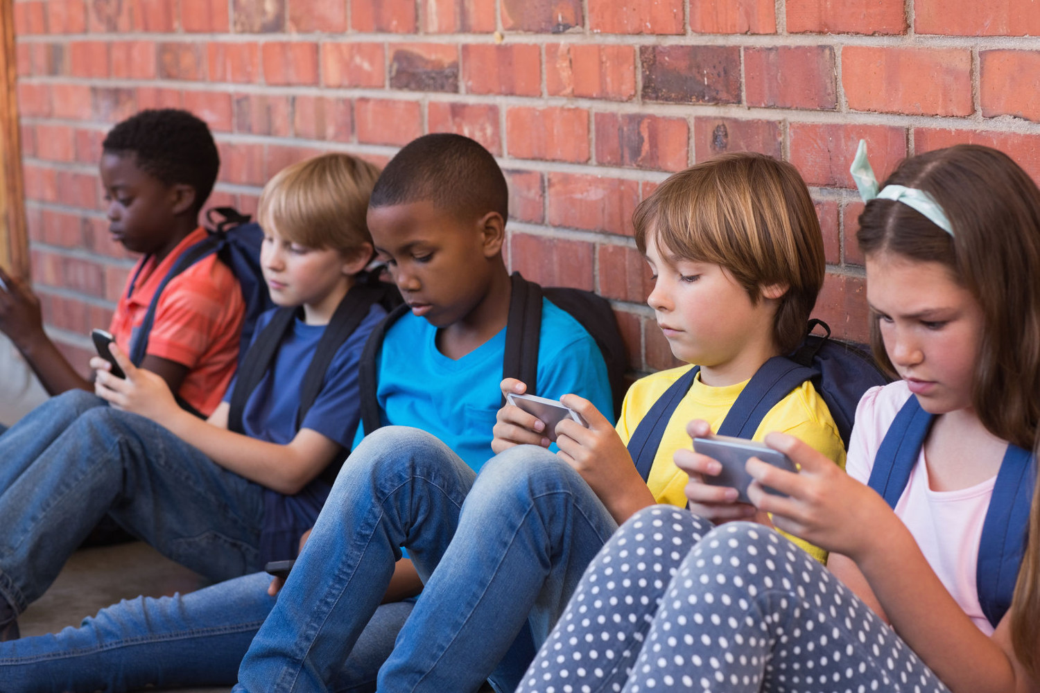 Group of children playing on smart phones against a brick wall