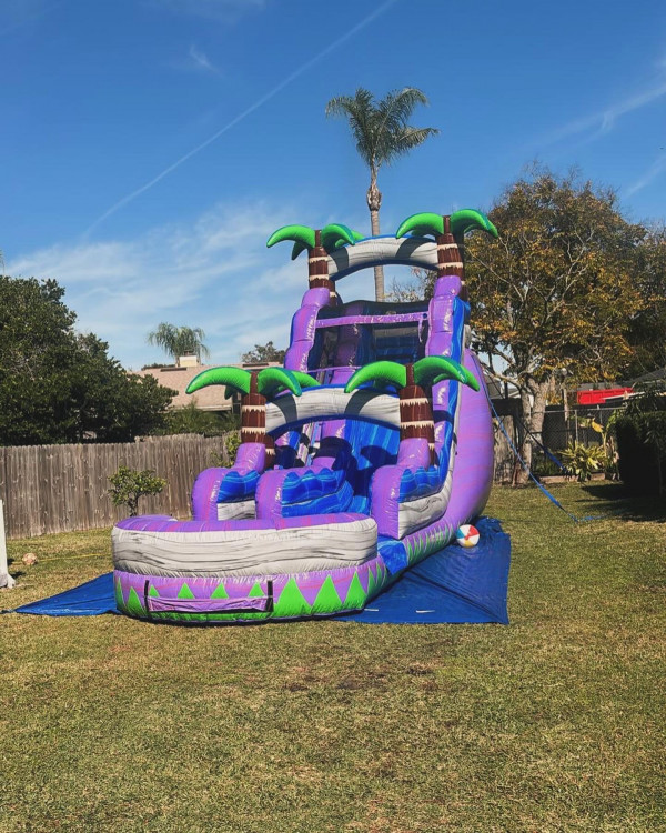 A purple and blue inflatable waterslide outside on green grass placed on blue tarp