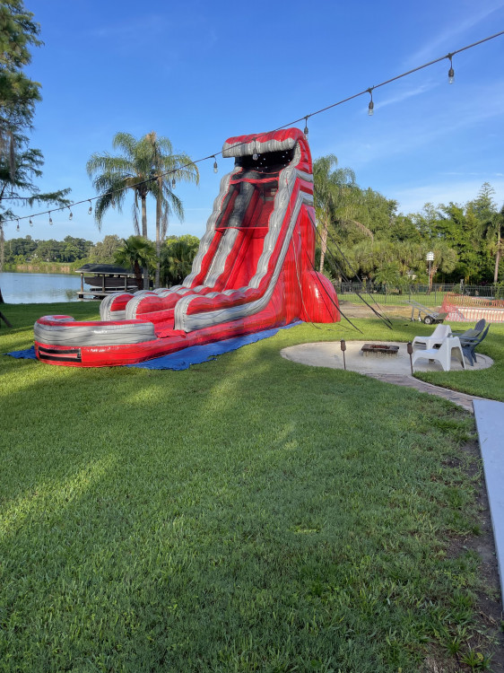 A tall inflatable water slide thats red and grey. Set up outside on green lushy grass.