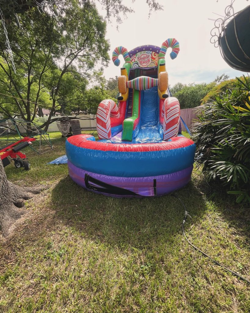 A giant colorful water slide with candy design, set up outside on a sunny day on green grass.