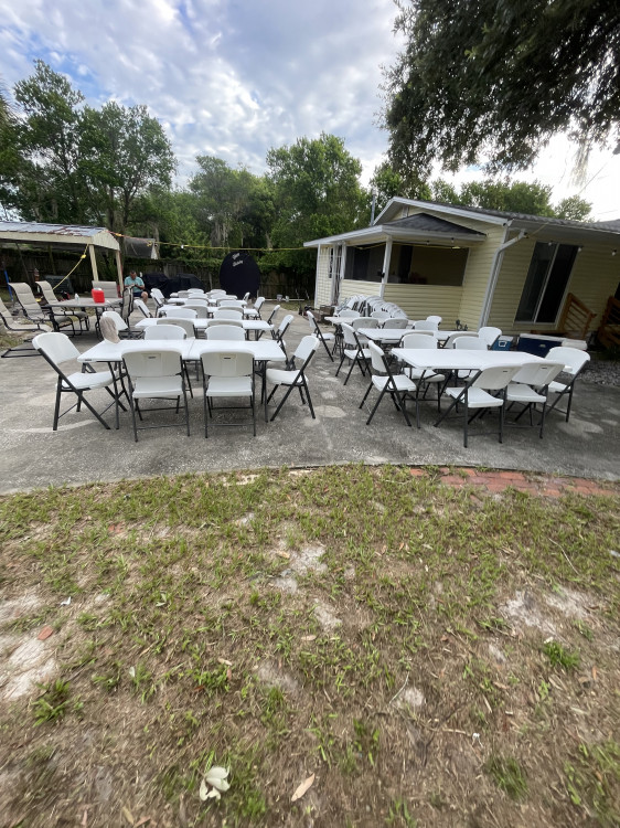 White Chairs and tables set up outside on concrete in a back yard of a house.