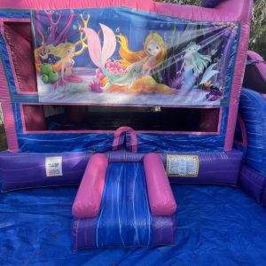 A pink and bright bounce house inflated on a blue tarp with a mermaid art panel around fun times bounce houses.