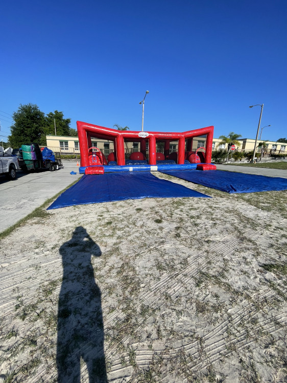 A large red and blue inflatable blown up Infront of a kid's school in parking lot outside on sunny day.