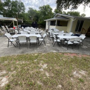 6FT Table Rental set up outside that are white with chairs around them