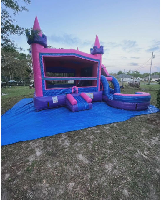 A pink girly bounce house set up outside on a blue tarp